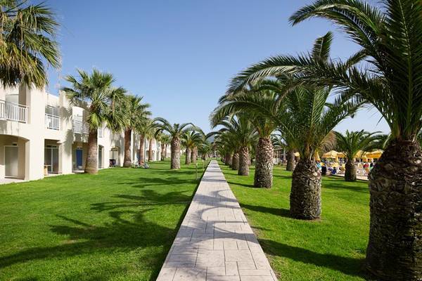 Palmen-Allee im Atlantica Holiday Village Kos, grüner Rasen und weiße Gebäude im Hintergrund.