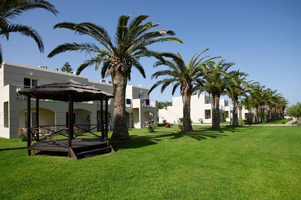 Außenbereich des Atlantica Holiday Village Kos mit Bungalows und Palmen.
