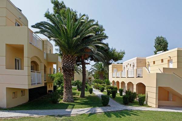 Außenbereich des Atlantica Holiday Village Kos mit Gebäuden, Palmen und Gehweg.