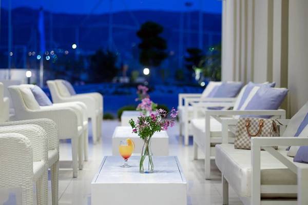 Loungebereich des Atlantica Holiday Village Kos mit weißen Möbeln und Blick auf einen Hafen.