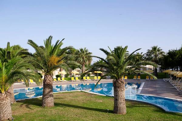 Außenpool des Atlantica Holiday Village Kos mit Palmen und Sonnenliegen.
