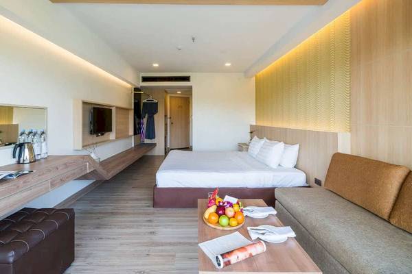 Hotelzimmer im Chaba Samui Resort mit Bett, Couch, Tisch, Fernseher und Früchten.
