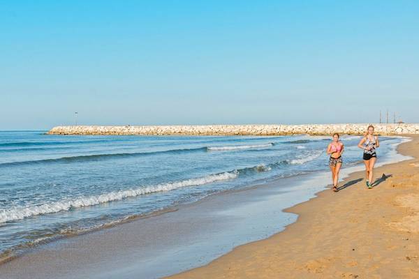 Zwei Frauen laufen am Strand entlang, der Ozean ist im Hintergrund zu sehen.