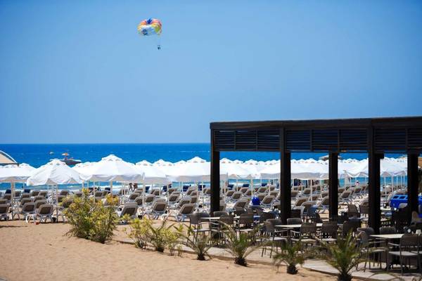 Strandszene mit vielen Sonnenschirmen und Liegen am Meer, ein Paraglider im Himmel