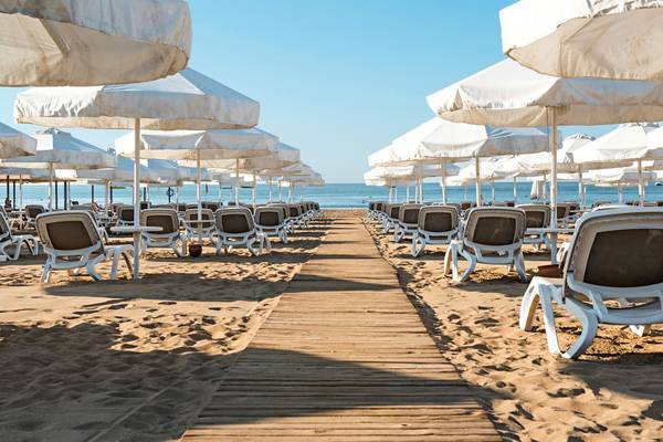 Reihe von weißen Sonnenschirmen und Liegestühlen auf einem sandigen Strandweg des Barut B Suites