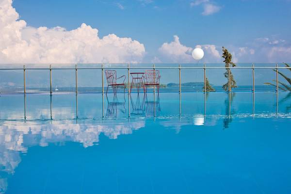 Ein Swimmingpool mit zwei roten Stühlen und einem Tisch, reflektiert unter einem blauen Himmel.
