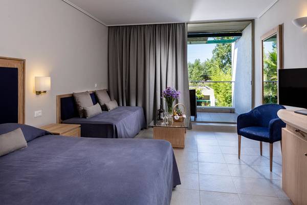 Hotelzimmer im Kontokali Bay Resort & Spa mit zwei Betten, einem Tisch, einer Tür zum Balkon und einem Fernseher.