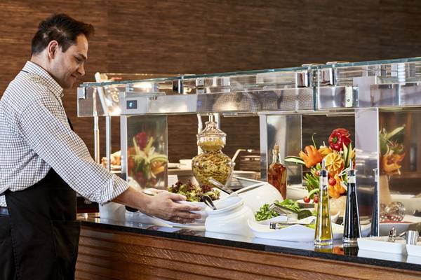 Mann bedient das Buffet im Hotel Kontokali Bay Resort & Spa mit Salaten, Dressings und Früchten.