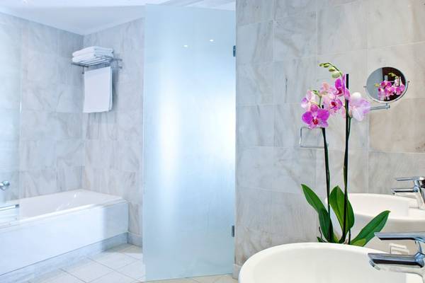 Badezimmer im Kontokali Bay Resort & Spa mit Badewanne, Waschbecken und Orchideenstrauß.