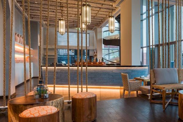 Inneneinrichtung der Lobby im Kempinski Hotel Muscat mit Holztischen, Stühlen und einer Bar.