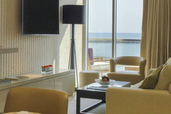Wohnbereich im Kempinski Hotel Muscat mit Meerblick, inklusive Fernseher, Tisch, Stühlen, Lampe und Couch.