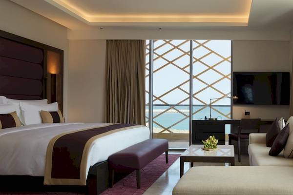 Innenansicht einer Suite im Kempinski Hotel Muscat mit Bett, Wohnzimmer, Fernseher und Meerblick.