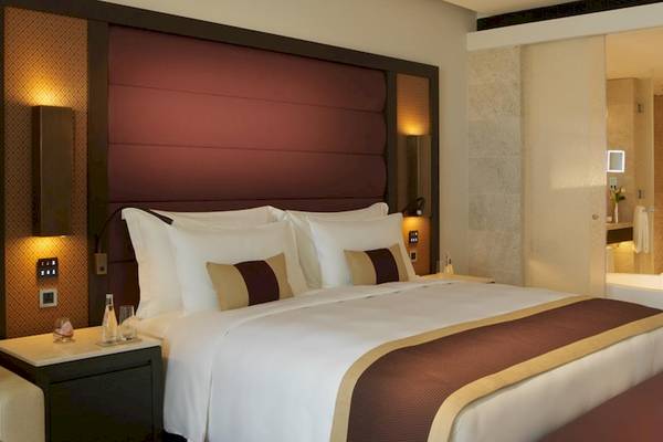 Luxuriöses Hotelzimmer im Kempinski Hotel Muscat mit großem Bett, Nachttischen und einem Badezimmer mit Badewanne.