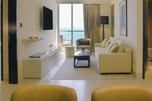 Luxuriöses Hotelzimmer mit Meerblick, inklusive Couch, Fernseher, Tisch und Balkonmöbel.