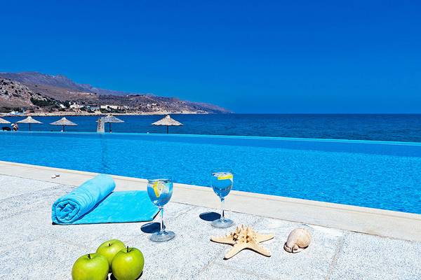 Ein Pool mit Blick auf den Strand und Erfrischungen wie Weingläsern, Äpfeln und einer Strandmuschel.