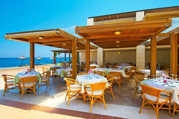 Terrasse des Giannoulis Grand Bay Beach Resort mit Tischen und Stühlen vor dem Meer