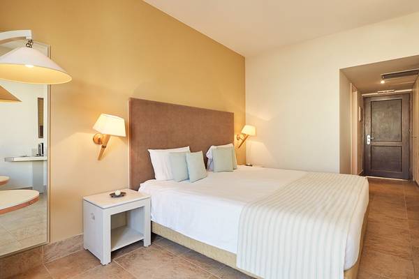 Doppelbettzimmer im Giannoulis Grand Bay Beach Resort mit beigefarbenen Wänden und einem gepolsterten Kopfteil.