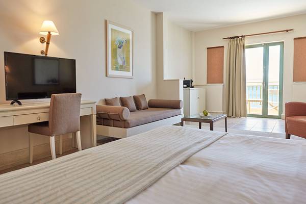 Zimmer im Giannoulis Grand Bay Beach Resort mit Fernseher, Schreibtisch und Sofa.