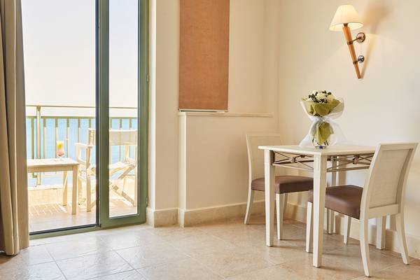 Innenraum mit Balkon, Tisch, Stühlen und Blumen auf dem Tisch, Blick auf das Meer.