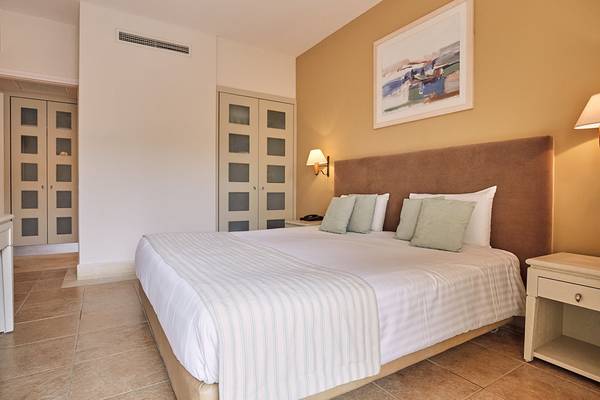 Hotelzimmer im Giannoulis Grand Bay Beach Resort mit Bett, Kissen, Nachttischen und Wanddekoration.