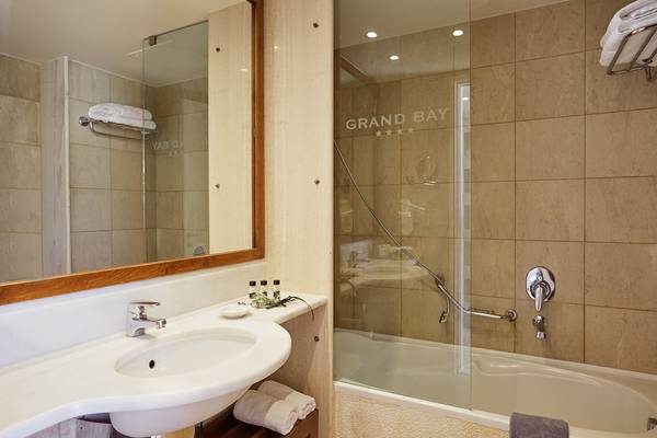 Badezimmer im Giannoulis Grand Bay Beach Resort mit Spiegel, Waschbecken und Badewanne.