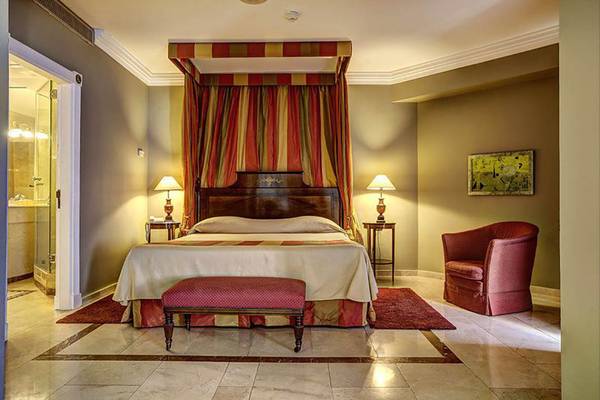 Schlafzimmer im Bull Hotel Reina Isabel mit einem großen Bett, einem Baldachin, einem roten Stuhl und zwei Tischlampen.
