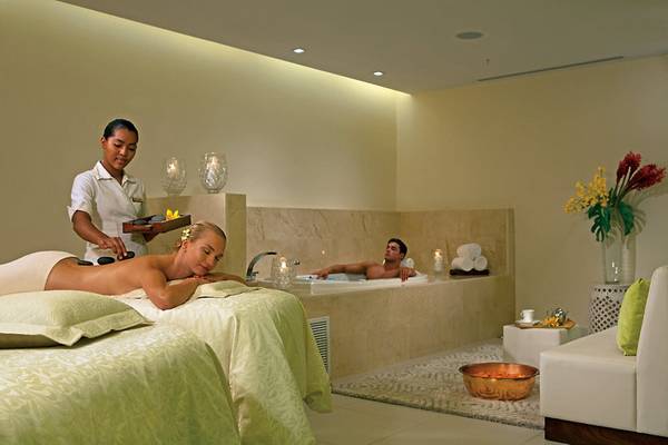 Massagebehandlung im Hotel Dreams Las Mareas Costa Rica mit einer Frau auf einer Liege und einem Mann im Whirlpool.