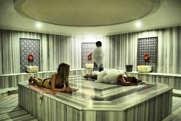 Im Tusan Beach Resort entspannen zwei Frauen in einer Sauna, während ein Mann Seifenschaum verteilt.