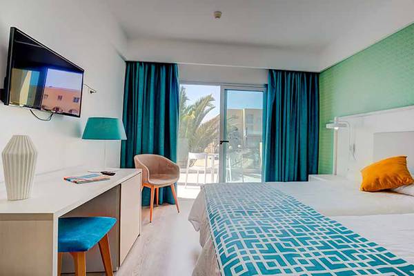 Innenansicht eines Doppelzimmers im SBH Maxorata Resort mit zwei Betten, Schreibtisch, Fernseher und Balkon.