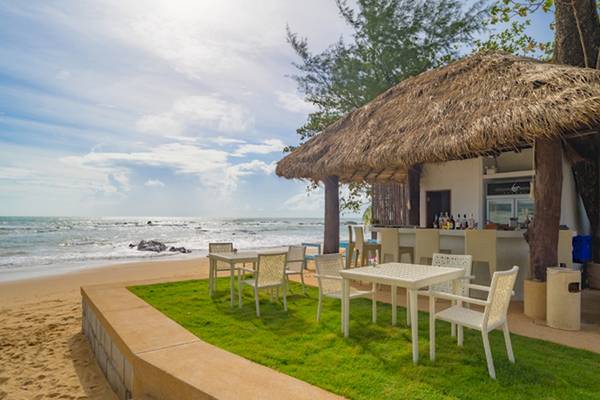Strandbar des Ocean Breeze Resort Khao Lak mit Tischen und Stühlen im Freien.