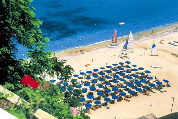 Luftaufnahme des Aldiana Club Rocca Nettuno Calabria mit vielen Sonnenschirmen und Segelbooten am Strand