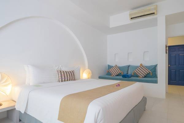 Innenansicht eines Schlafzimmers im Ocean Breeze Resort Khao Lak, mit einem großen Bett, weißen Wänden und einer blauen Fensterbank.