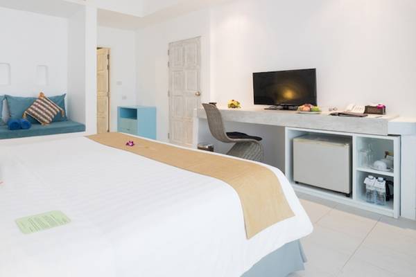 Innenansicht eines Zimmers im Ocean Breeze Resort Khao Lak mit einem Bett, Fernseher, Schreibtisch und blauem Sofa.