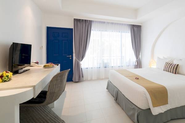 Ein modernes Hotelzimmer im Ocean Breeze Resort Khao Lak mit weißem Bett, blauer Tür und Fenster.