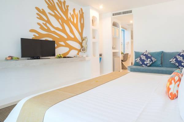 Innenansicht eines Hotelzimmers im Ocean Breeze Resort Khao Lak mit einem Bett, Fernseher und Dekor.
