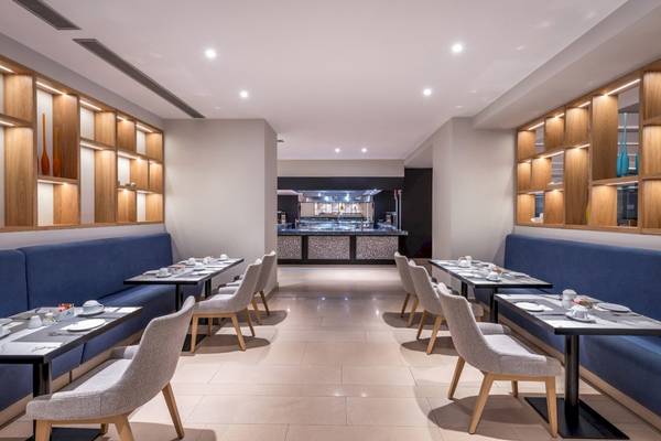 Innenansicht des Restaurants im Mitsis Rodos Village Beach Hotel & Spa mit gepolsterten Bänken, gedeckten Tischen und einer offenen Küche.