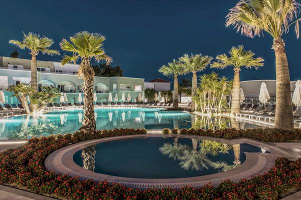 Nachtansicht des Pools im Mitsis Rodos Village Beach Hotel & Spa mit Palmen und Blumen.
