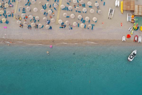 Luftaufnahme des Mitsis Rodos Village Beach Hotel & Spa am Strand mit vielen Liegen, Sonnenschirmen und Wassersportgeräten.