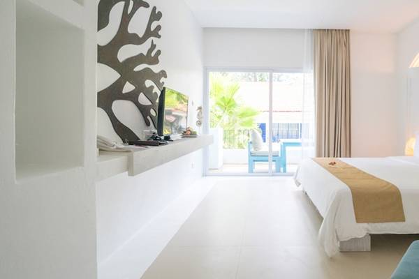Ein modernes Hotelzimmer im Ocean Breeze Resort Khao Lak mit weißem Bett, Kissen, Fernseher und offenem Balkon.