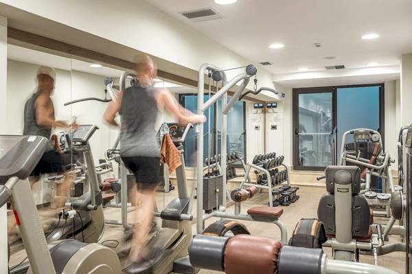 Fitnessstudio im Mitsis Rodos Village Beach Hotel mit verschiedenen Geräten und zwei Personen, die Cardiogeräte benutzen.