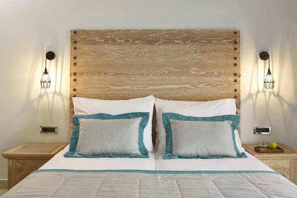 Schlafzimmer im Mitsis Rodos Village Beach Hotel mit Holzkopfteil, weißen Kissen und blauen Kissenbezügen.