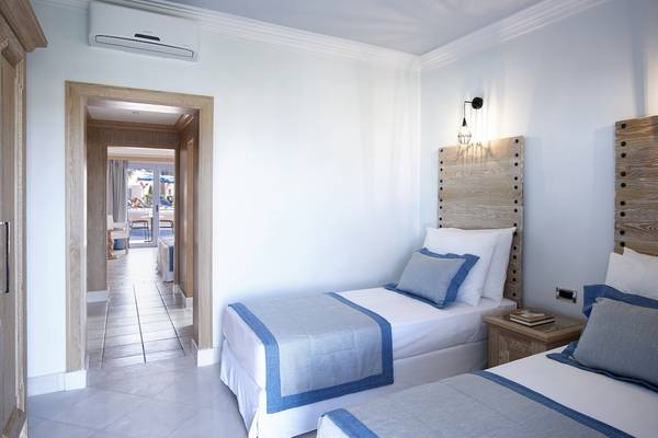 Schlafzimmer im Mitsis Rodos Village Beach Hotel mit zwei Betten, hölzernem Kopfteil und Klimaanlage.