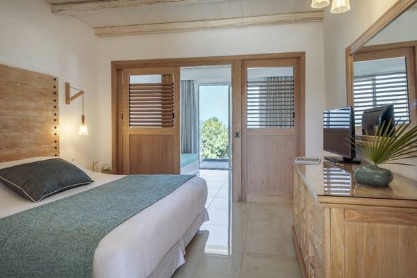 Innenansicht eines Schlafzimmers im Mitsis Rodos Village Beach Hotel mit einem Bett, einem Fernseher und einem offenen Fenster.