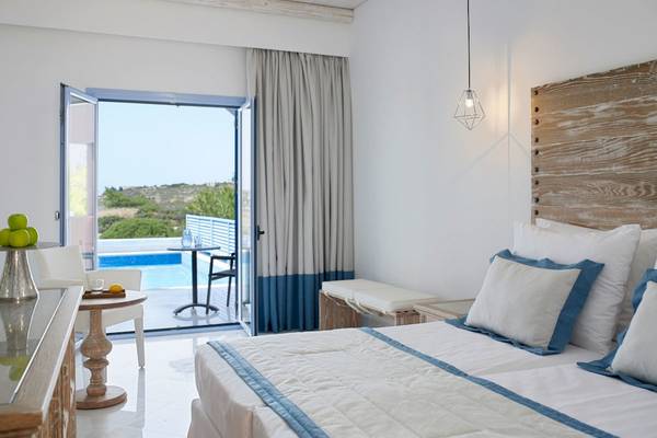 Innenansicht eines Schlafzimmers im Mitsis Rodos Village Beach Hotel mit Blick auf einen Pool und eine Terrasse.
