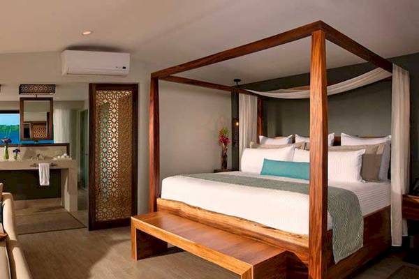 Luxuriöses Hotelzimmer im Secrets Papagayo Costa Rica mit Baldachinbett, Sofa und Badezimmer mit Badewanne.