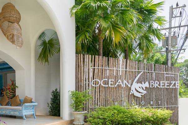 Eingang zum Ocean Breeze Resort Khao Lak mit weißem Gebäude, blauer Couch und tropischen Pflanzen