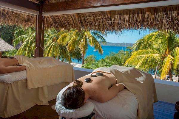 Zwei Personen erhalten eine Massage mit heißen Steinen auf einer Terrasse mit Blick auf das Meer im Hotel Secrets Papagayo Costa Rica.
