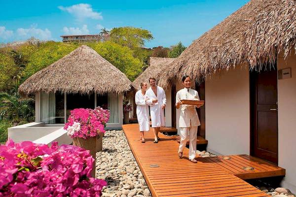 Gäste des Secrets Papagayo Costa Rica Hotel gehen auf einem Holzweg vorbei an Hütten.