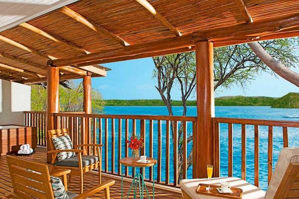 Balkon mit Meerblick im Secrets Papagayo Hotel, Costa Rica, mit Holzmöbeln, einem kleinen Tisch und Ausblick auf das Meer.