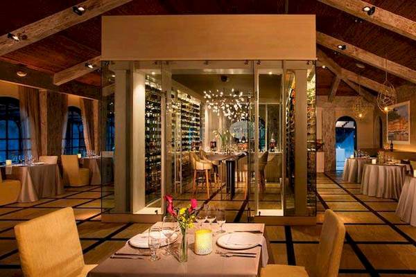 Innenbereich des Restaurants im Secrets Papagayo Costa Rica mit mehreren Tischen und Stühlen, einer großen Glaswand, Weinregal und dekorativen Lampen.